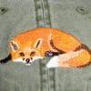 A close up of an embroidered fox on the back of a green jacket.