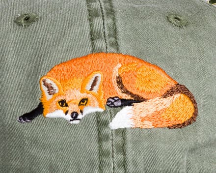 A close up of an embroidered fox on the back of a green jacket.