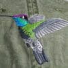 A hummingbird is embroidered on the back of a green shirt.