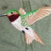 A hummingbird is embroidered on the back of a green jacket.