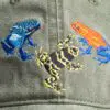 A close up of three different colored frogs on a hat