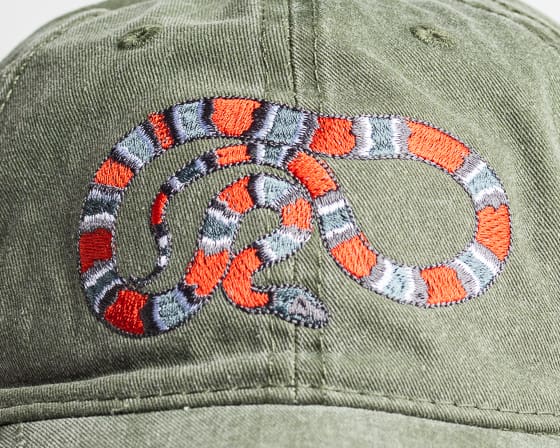 A close up of the back of a hat with an orange and grey snake on it