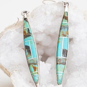 A pair of turquoise and silver earrings sitting on top of a rock.