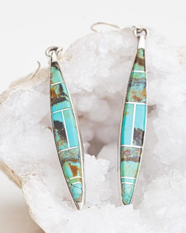 A pair of turquoise and silver earrings sitting on top of a rock.