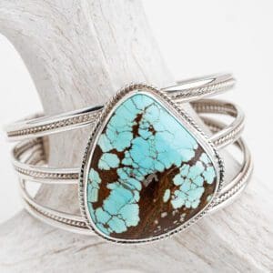A turquoise stone is sitting on top of a silver bracelet.