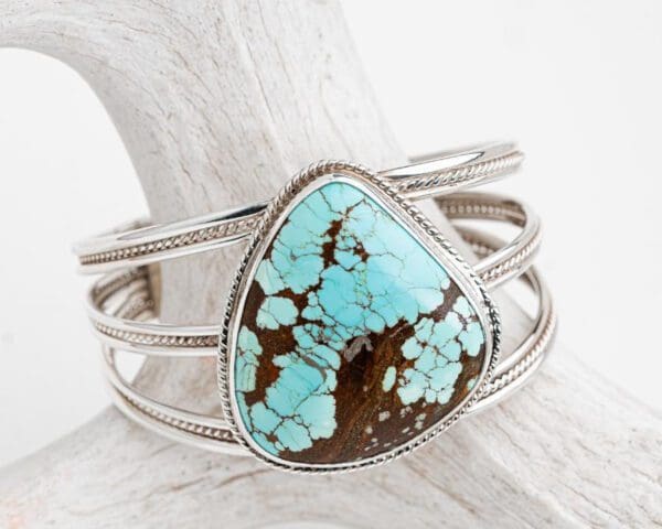 A turquoise stone is sitting on top of a silver bracelet.