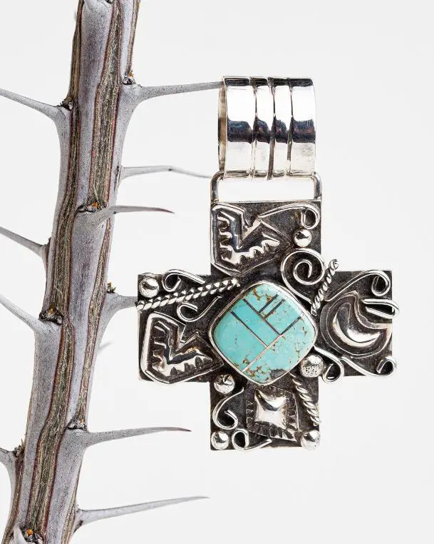 A cross shaped pendant hanging on top of a tree branch.