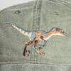 A close up of the back of a hat with an embroidered dinosaur.