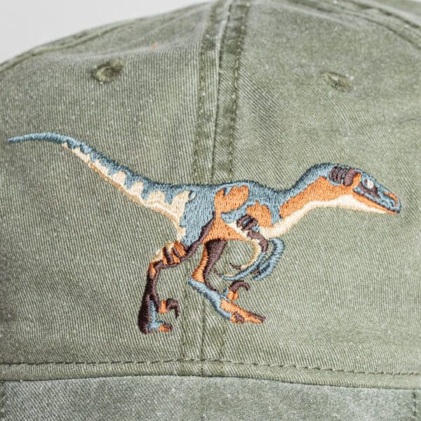 A close up of the back of a hat with an embroidered dinosaur.