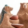 Three bears are sitting in a group and one is holding a bowl.