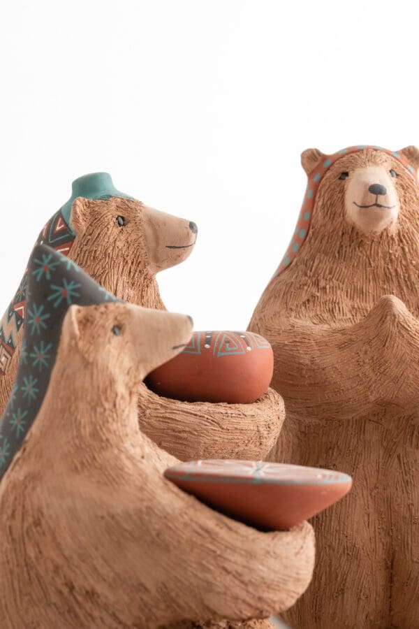 Three bears are sitting in a group and one is holding a bowl.