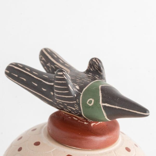 A bird figurine sitting on top of a ceramic vase.