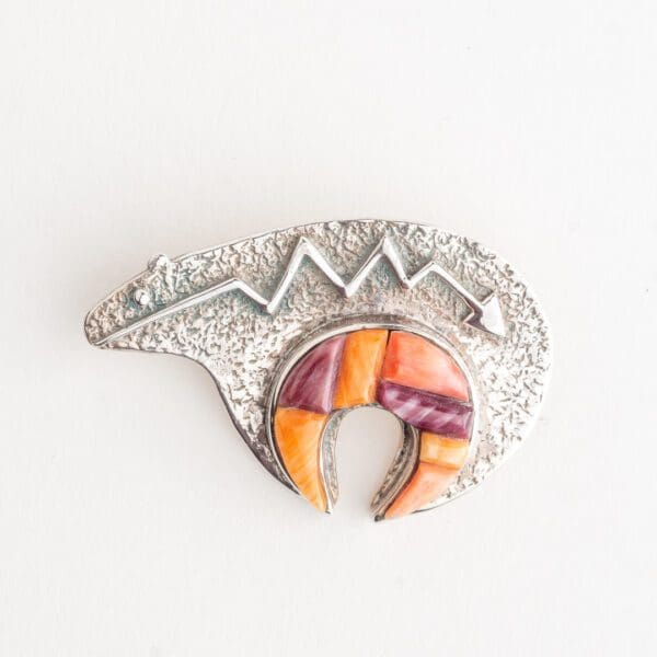 A silver brooch with a colorful design on it.