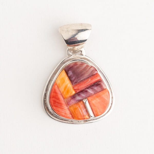 A silver pendant with an orange and purple design.